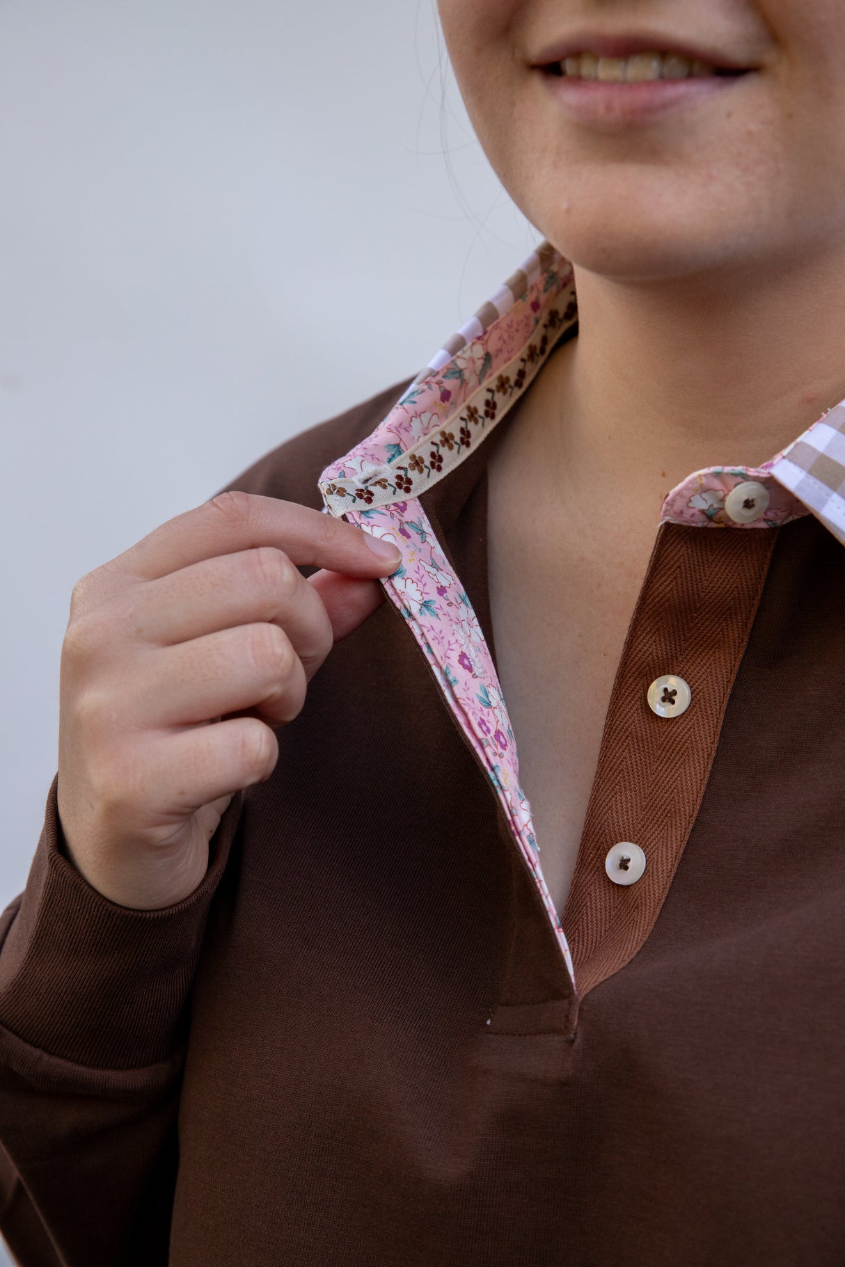 Close-up of a woman wearing a chocolate brown rugby shirt with a floral collar against a plain background