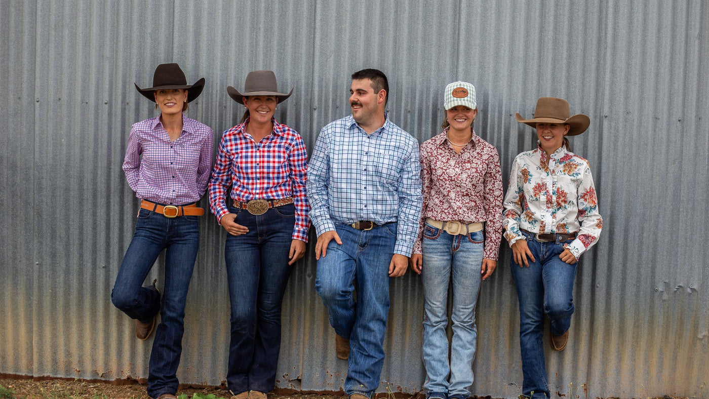 Men and Women wearing cotton shirts, denim jeans, cowboy hats and casual clothing standing against a corrugated metal wall.