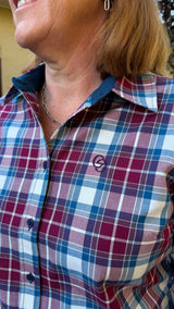 Close-up of a woman wearing a plaid button-up shirt in burgundy, blue, and white, with a small embroidered circular logo on the chest.