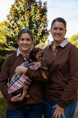 Two ladies wearing chocolate brown rugby shirts with a dog in a plaid blanket outdoors.