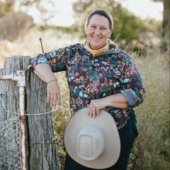 Woman standing by a wooden fence holding a hat in a natural setting